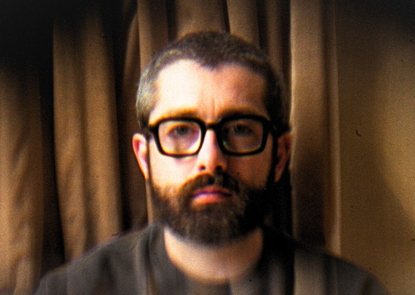 Man with glasses posing infront of curtainx
